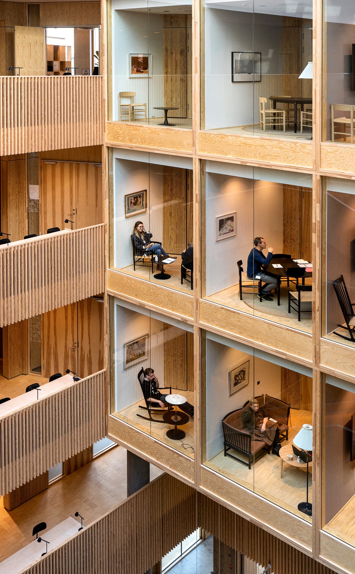 Modern office interior with multi-level glass-walled workspaces featuring wood panels and residential-style furnishing