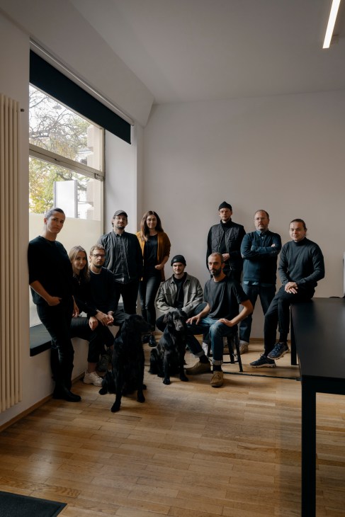The Herburg Weiland team of ten staff members posing together in their Munich studio with large windows and wooden flooring.