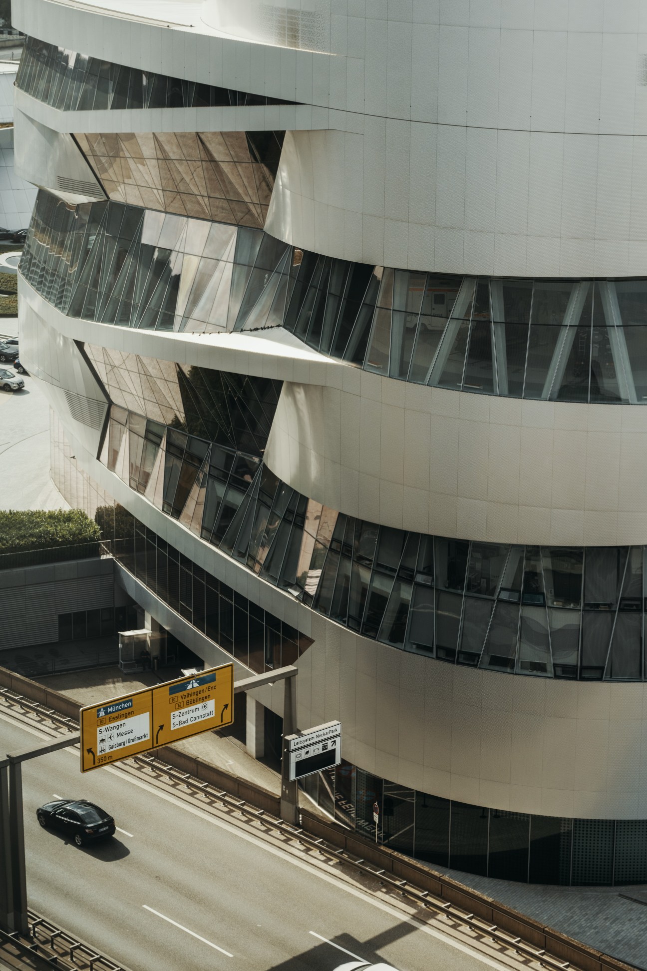 Modern cylindrical white building with curved balconies and dark windows, a car parked below.
