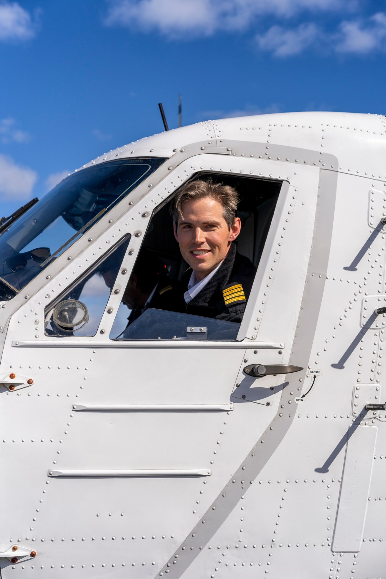 Seaplane captain Lasse Rungholm in cockpit of white Twin Otter aircraft wearing black suit with golden epaulettes.