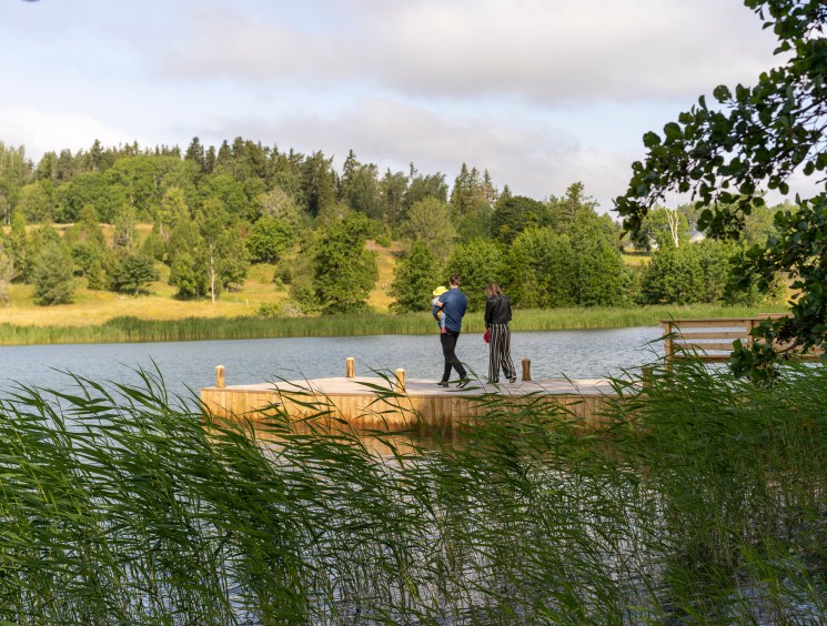 Two people standing on wooden dock extending into lake with forested hills in background