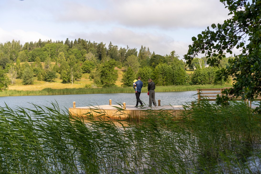 Two people standing on wooden dock extending into lake with forested hills in background