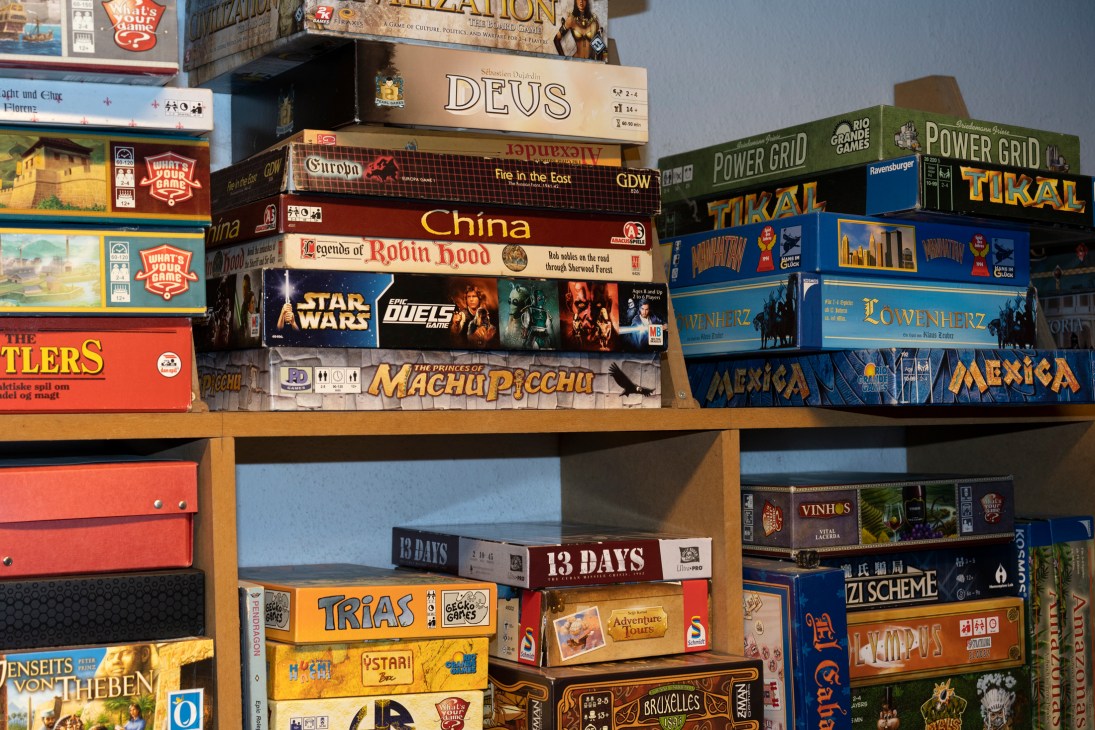 Shelves filled with colorful board game boxes stacked together, showing various game titles and cover art.