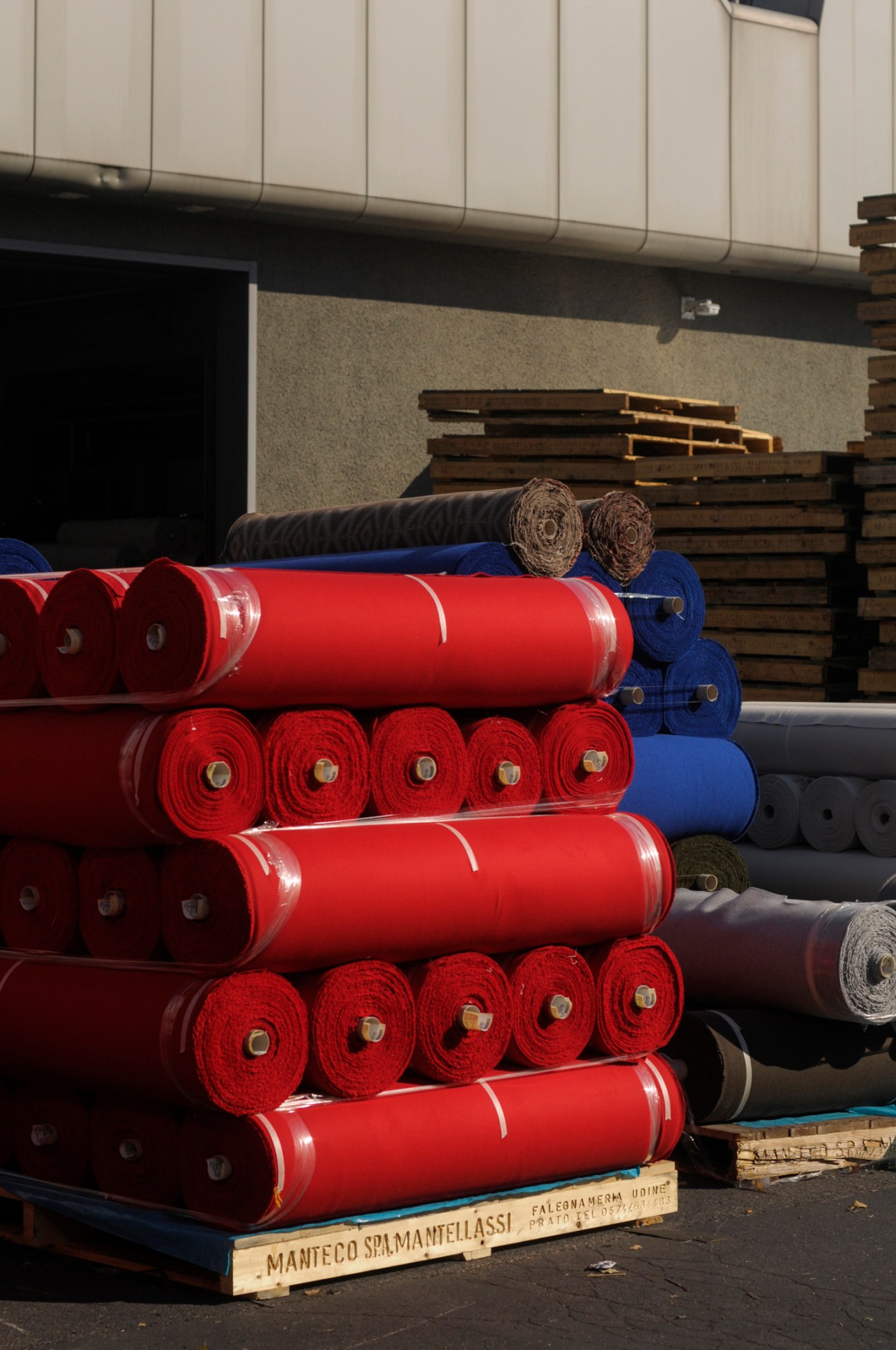 Stacked rolls of red, blue and other colored recycled wool fabric in warehouse with wooden pallets