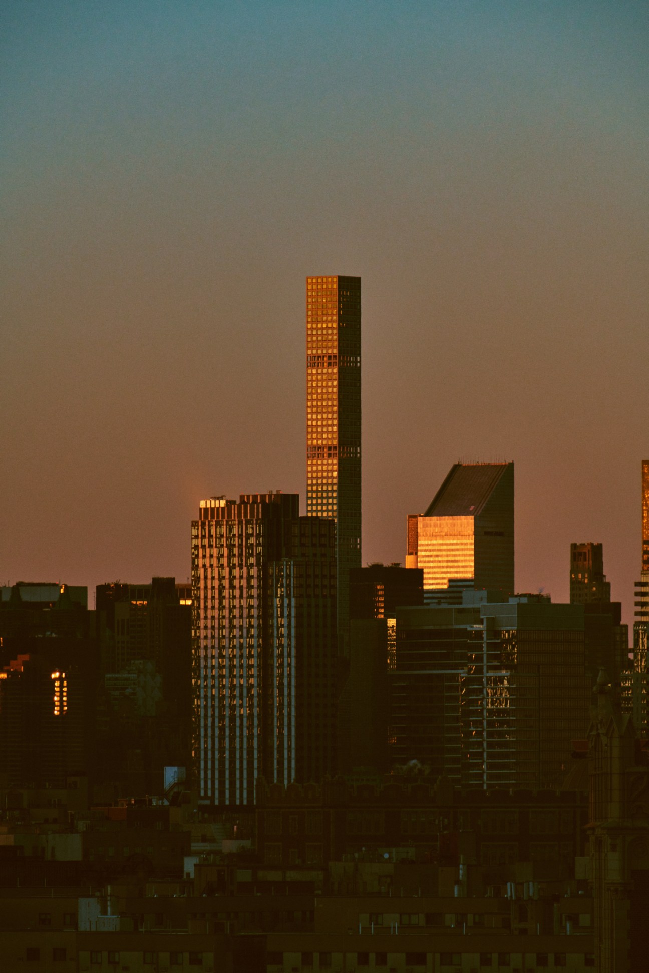 New York City skyline at sunset with illuminated skyscrapers against a dusky sky.