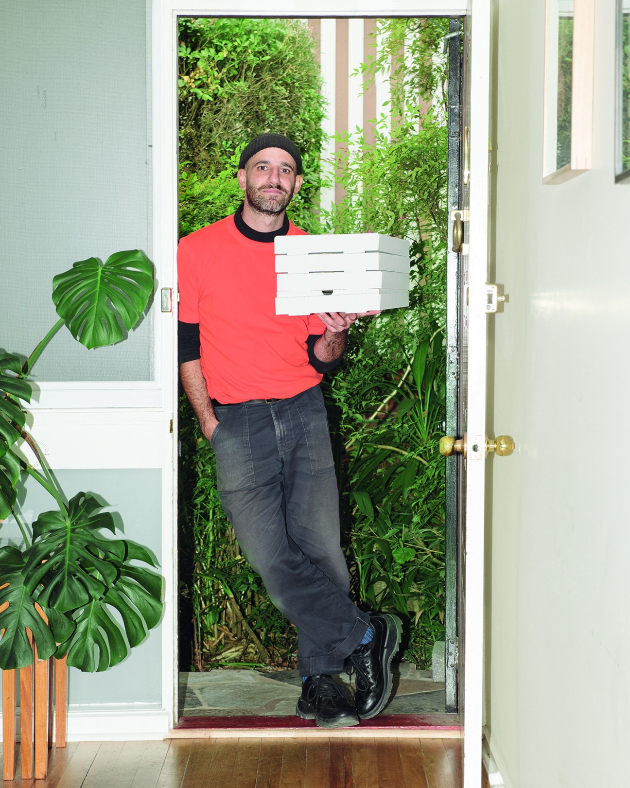 Delivery driver holding pizza boxes stands at doorway during pandemic isolation photography series.