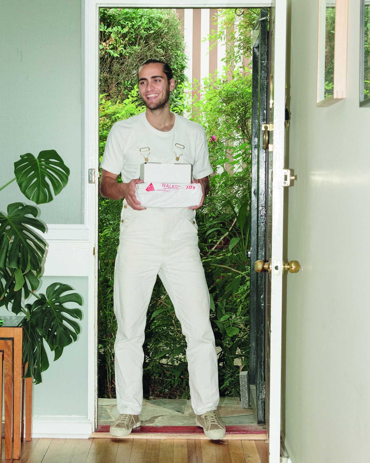 Delivery driver in white uniform holding package at residential doorway during pandemic isolation.