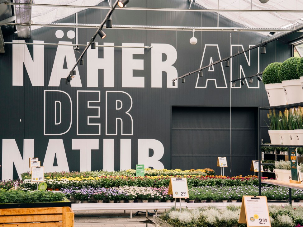 Kremer garden centre interior with flowering plants displayed against dark wall signage.