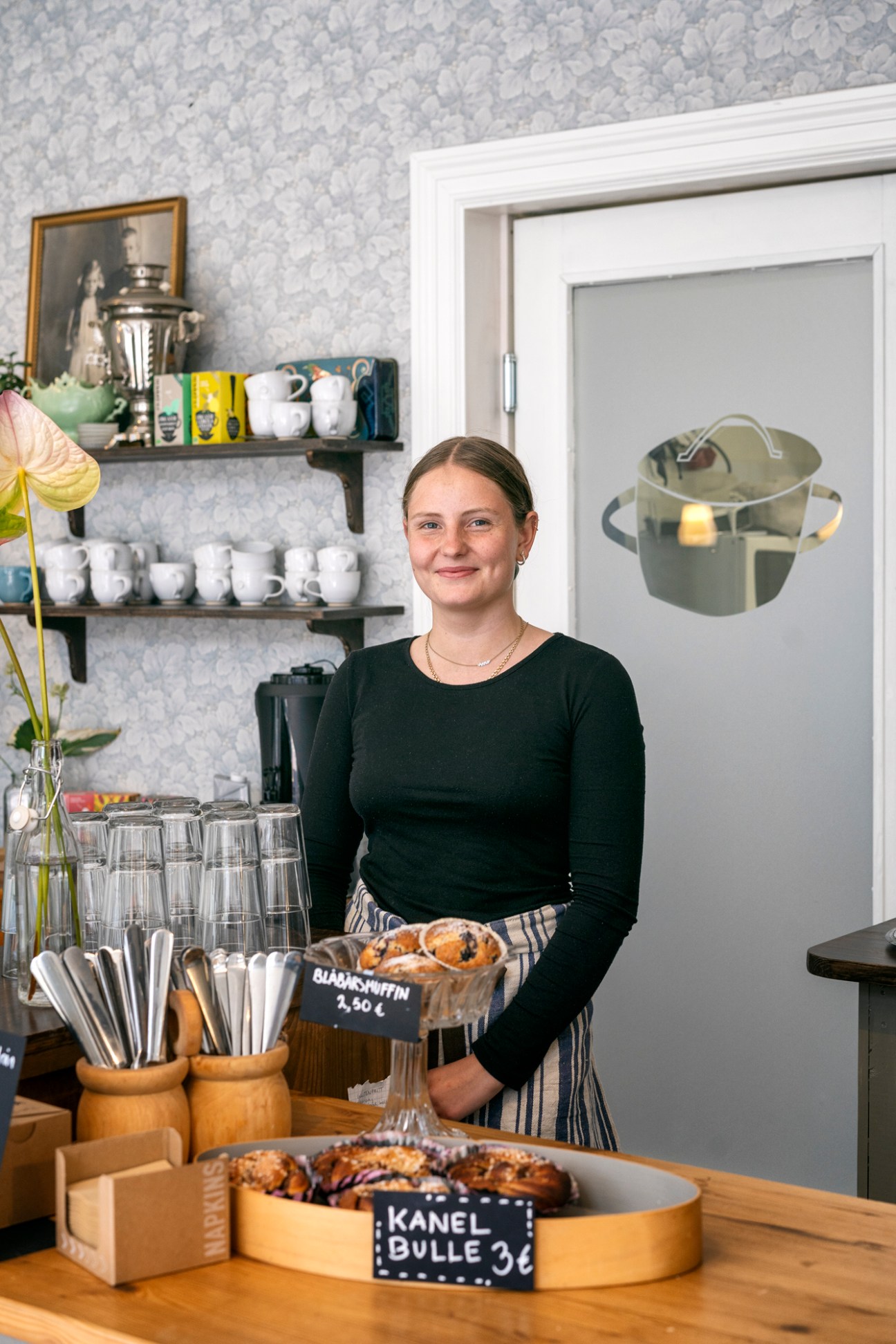 Woman in black sweater standing behind counter with pastries at Viktor Crafts & Design cafe interior