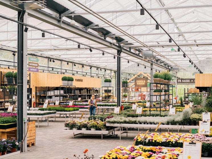 Interior of Kremer garden centre in Lennestadt showing glass greenhouse structure with organized plant displays and wooden market stalls.