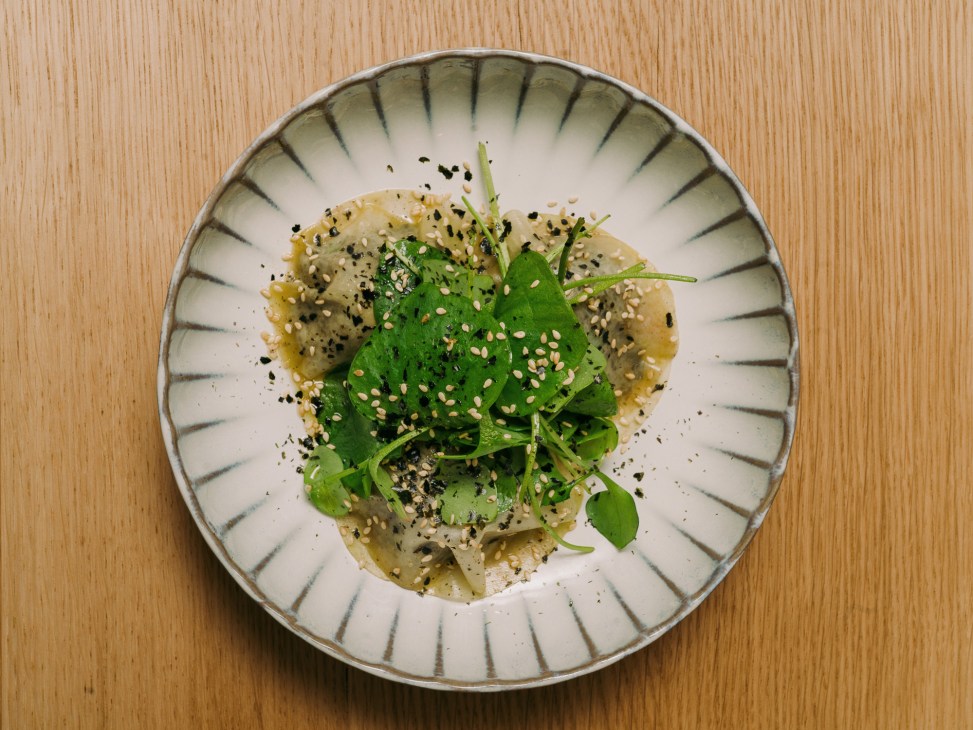 Ravioli of raw kohlrabi, confit algues and apples garnished with sesame seeds and herbs in a fluted ceramic bowl