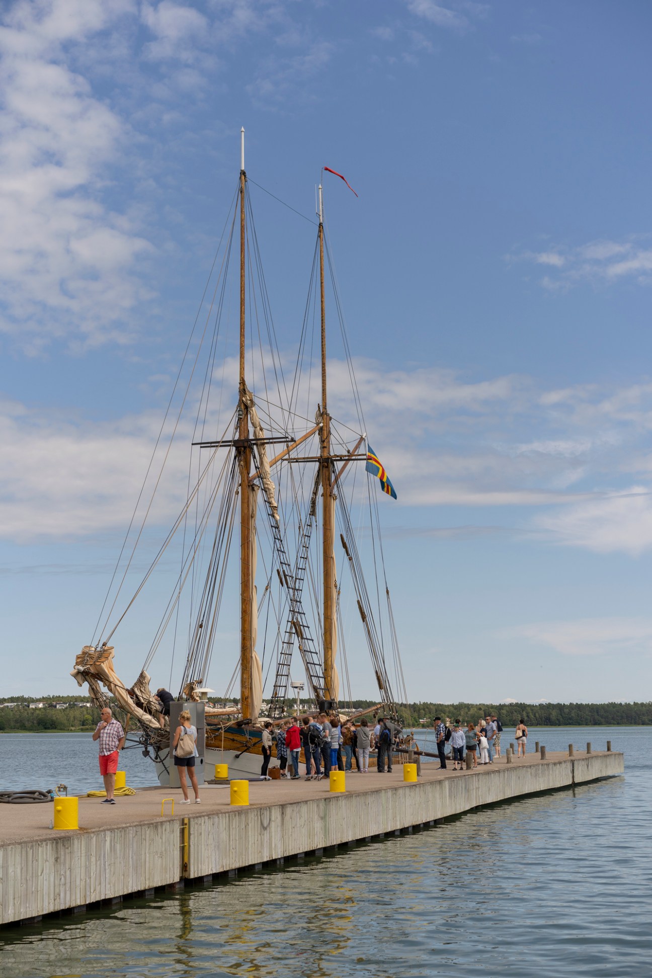 Historic tall ship with two masts and rigging docked at pier with visitors gathered on wooden dock
