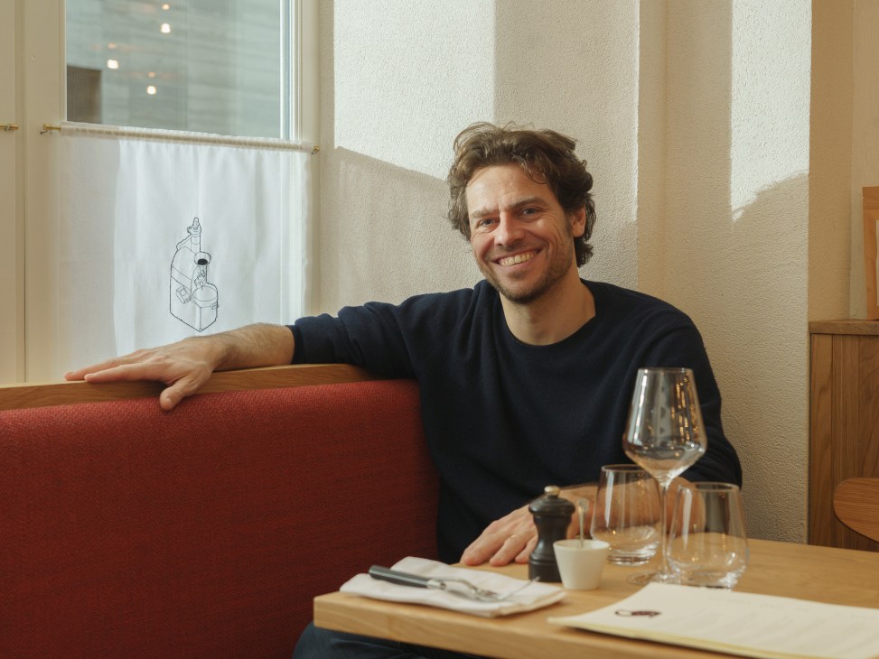 Charles Compagnon smiling while seated at a restaurant table with wine glass and coffee cup