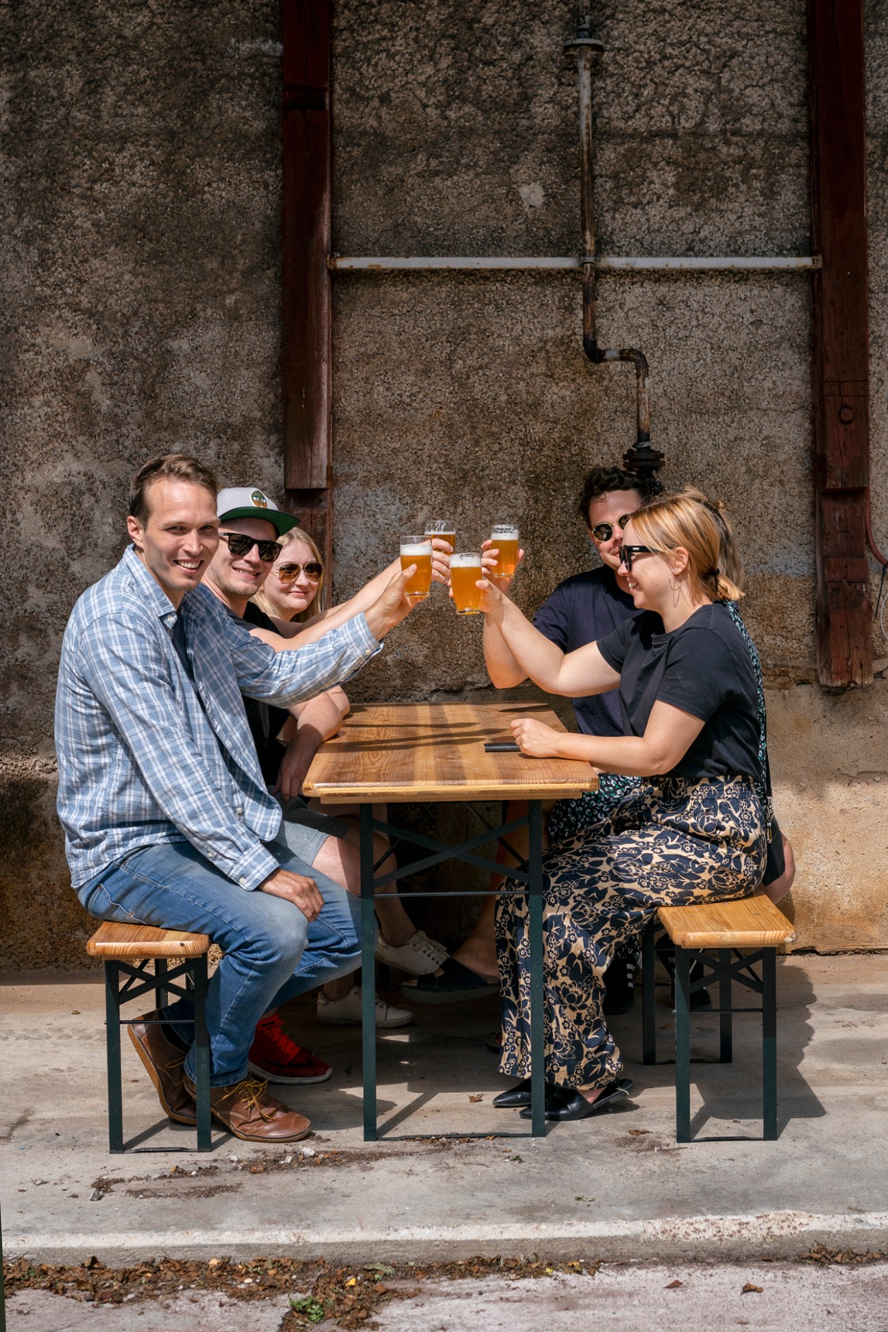 Five people sitting at outdoor wooden table raising beer glasses in cheers at Open Water Brewery