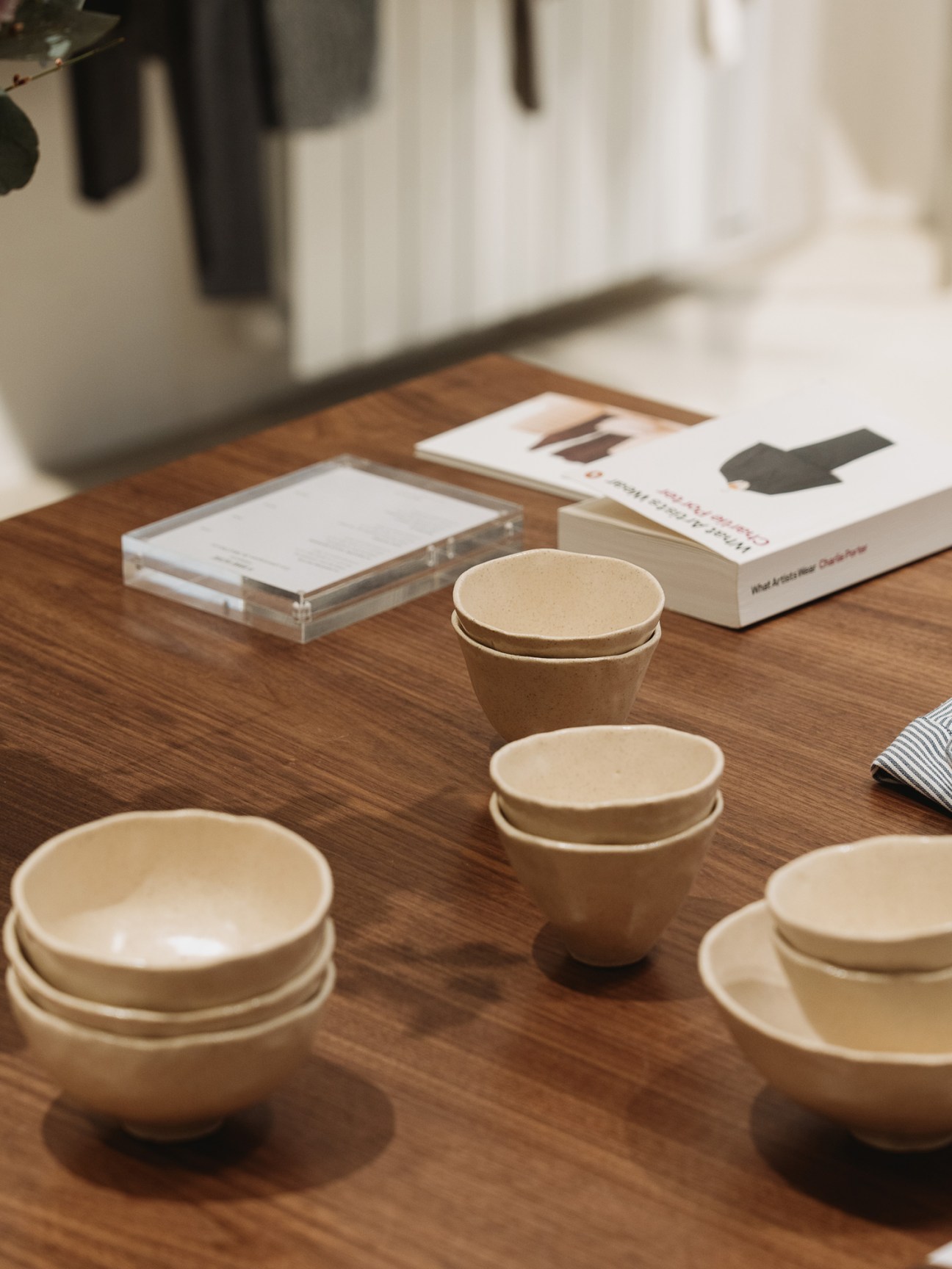 Beige ceramic bowls and cups arranged on a wooden table with books in the background
