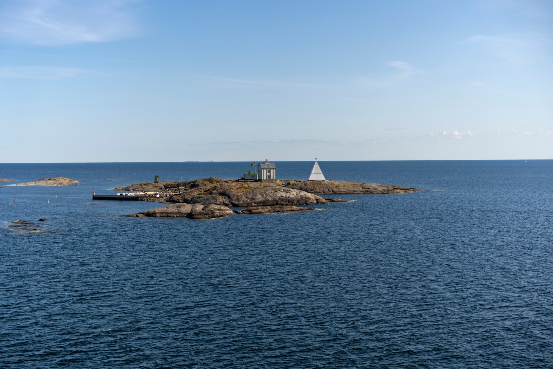 Rocky island with white lighthouse structure and triangular marker surrounded by blue Baltic Sea waters