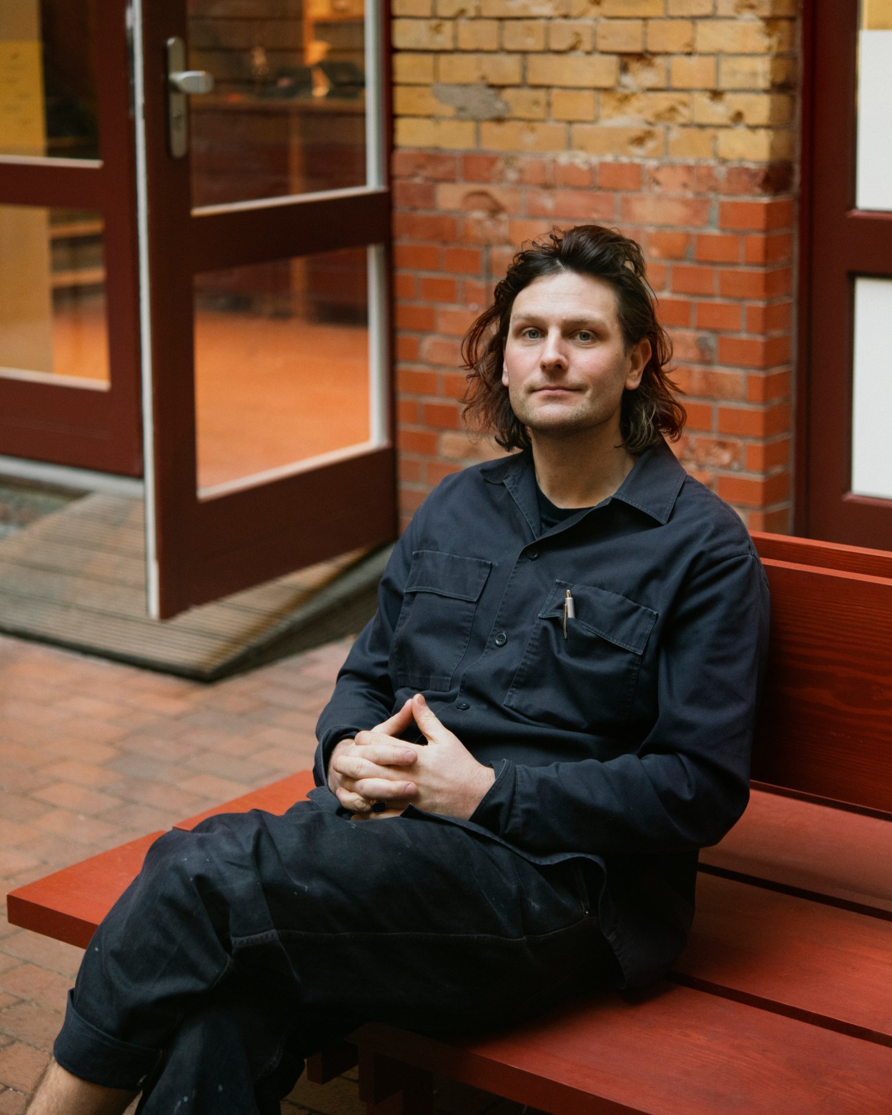 Chef Frederik Bille Brahe sitting on orange steps wearing dark work clothes at Sofi bakery in Berlin