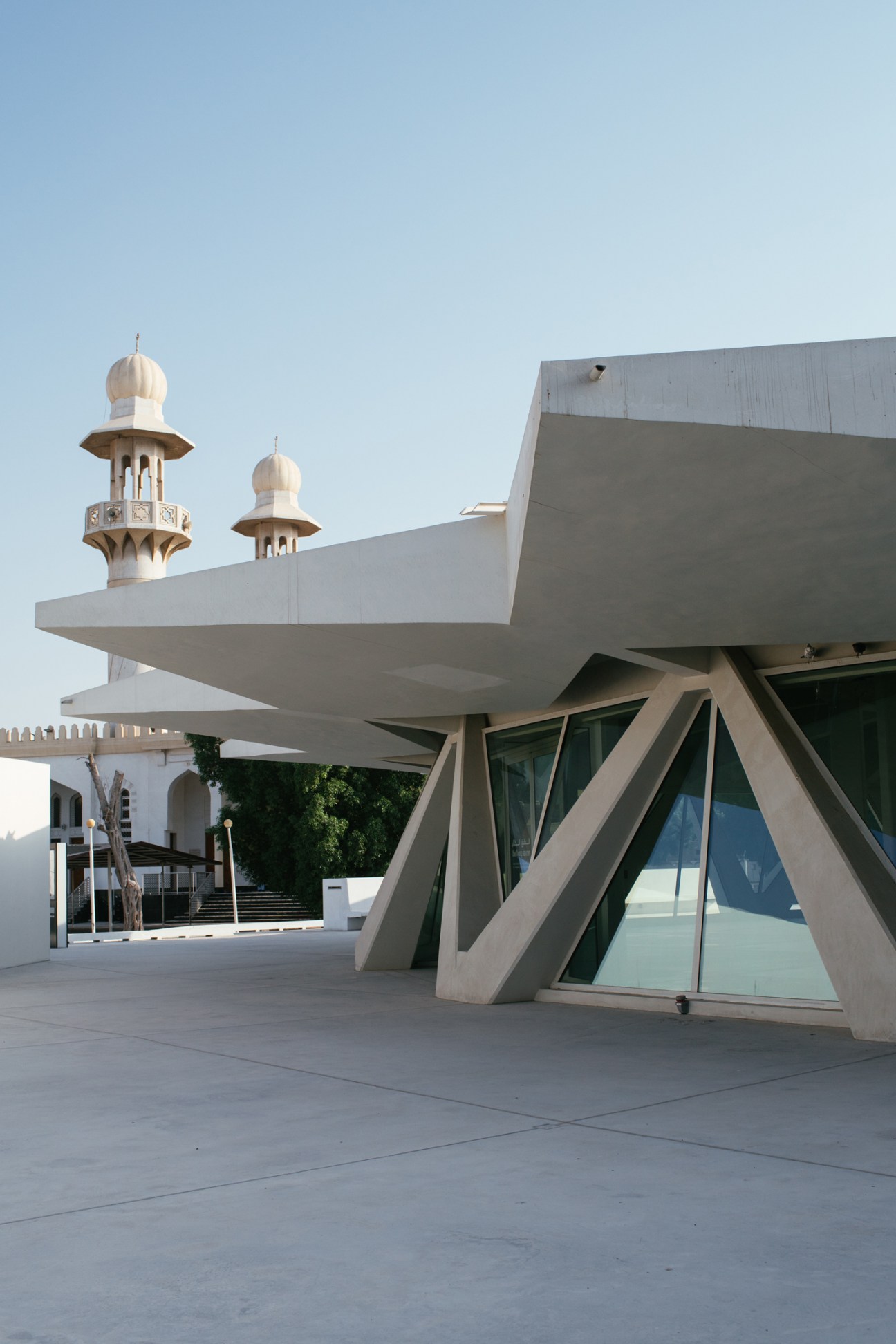 Modern architectural structure with white concrete canopy beside traditional mosque with domed minarets in Sharjah