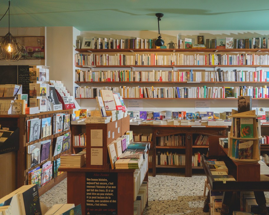 Interior of L'impromptu bookshop with floor-to-ceiling bookshelves and books displayed on tables
