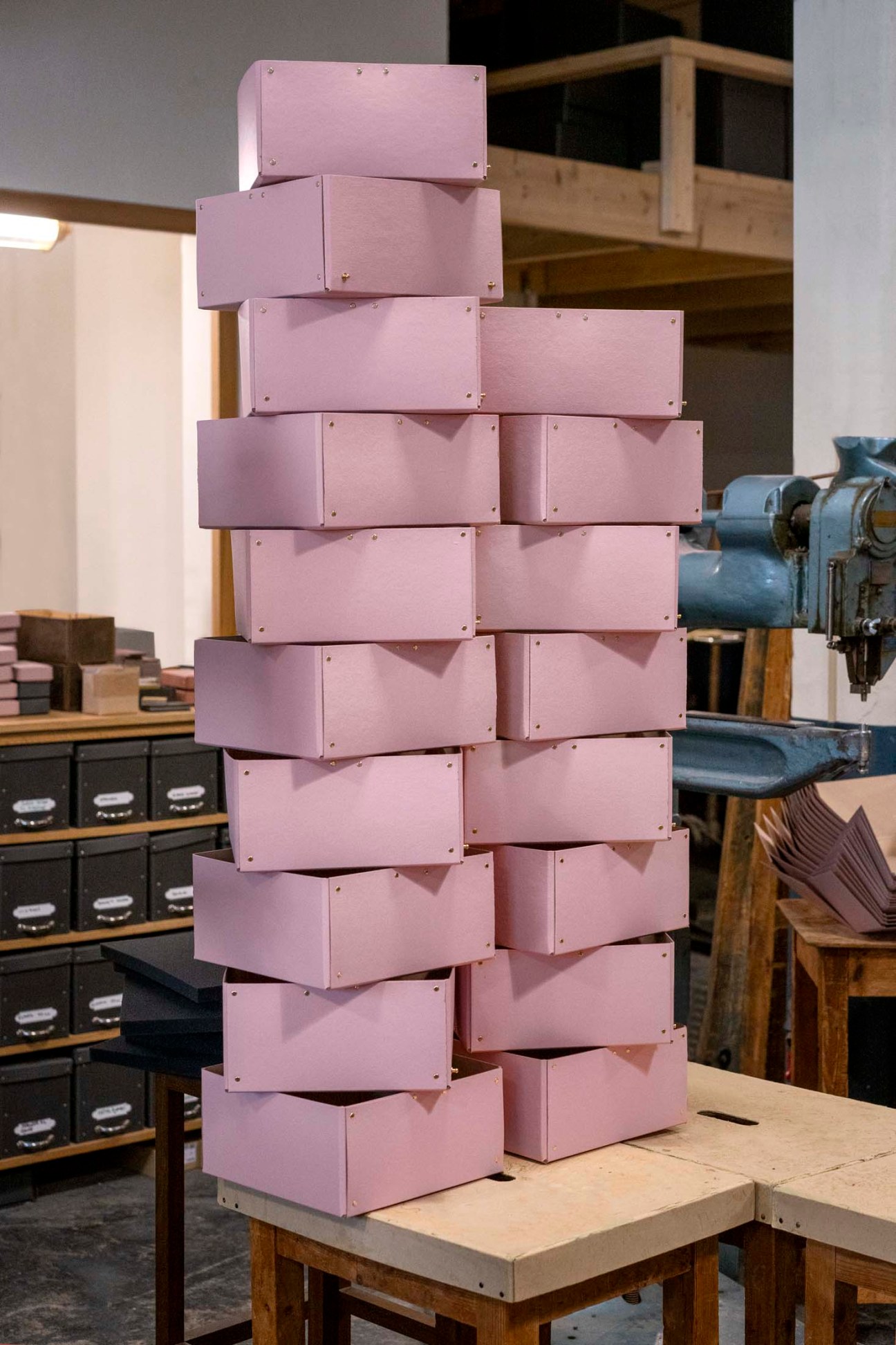 Stacked pink cardboard boxes with metal fasteners displayed in a workshop.