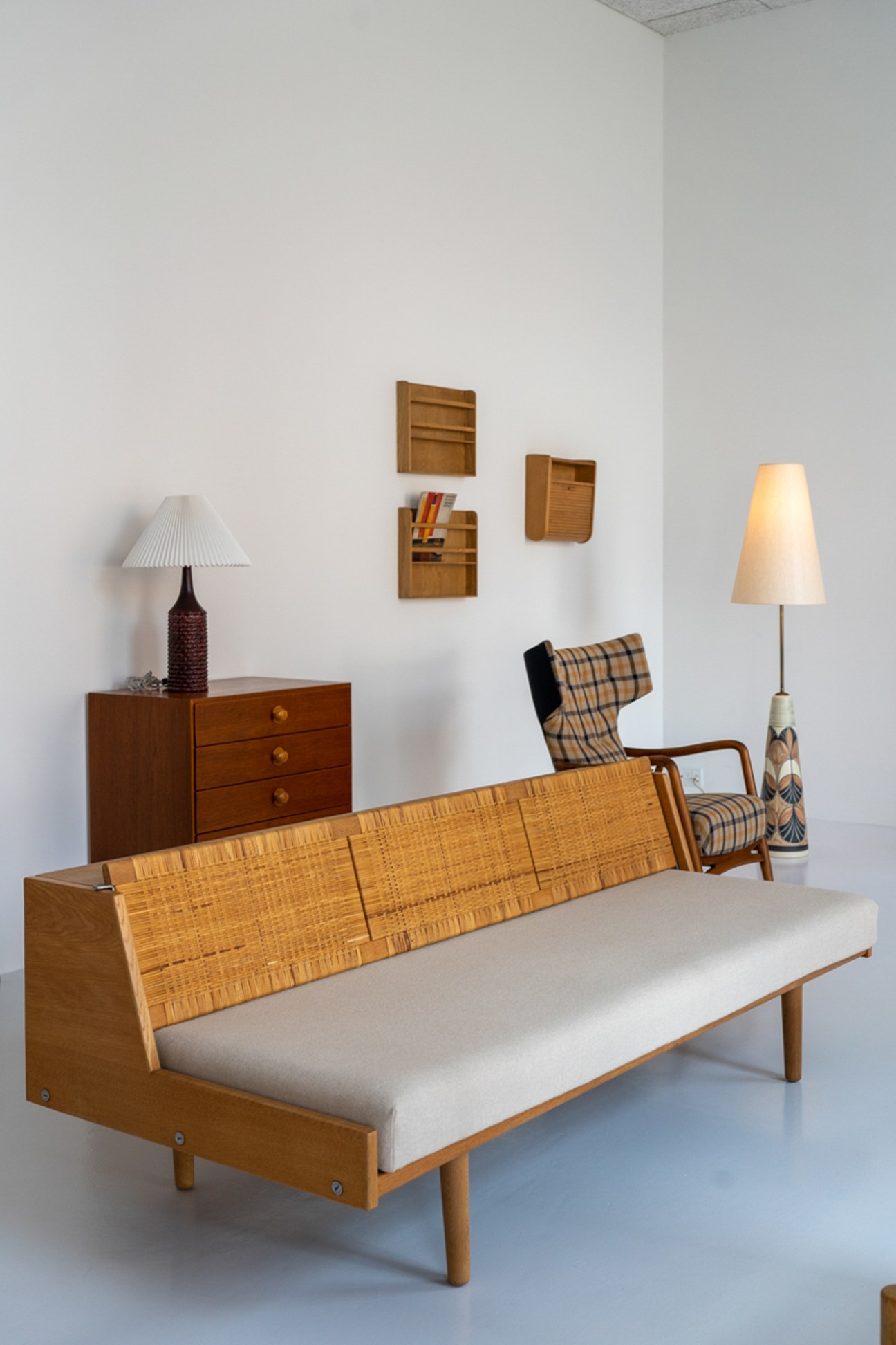 Mid-century Danish furniture display featuring woven wood daybed, chest of drawers, and modernist lighting
