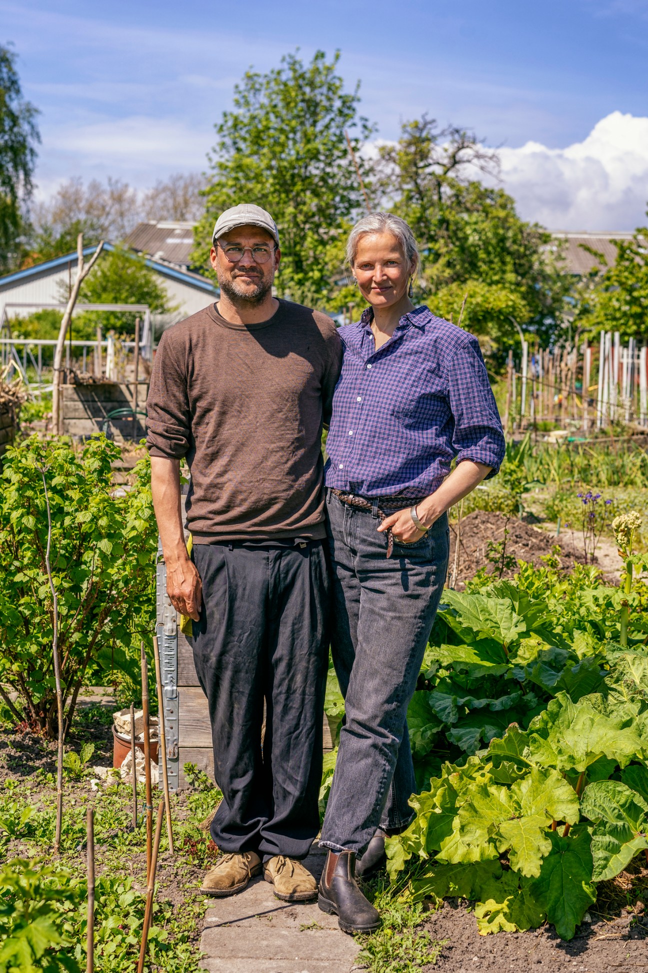 Ebbe Stub Wittrup and Lotte Bank Nielsen standing together in their allotment garden with vegetables and greenhouse