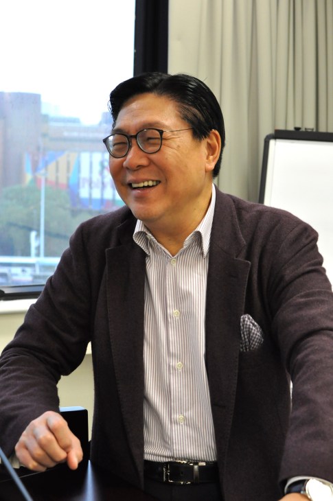 Frederick Ma, chairman of MTR, smiles during an interview in an office with Hong Kong cityscape visible through windows behind him.