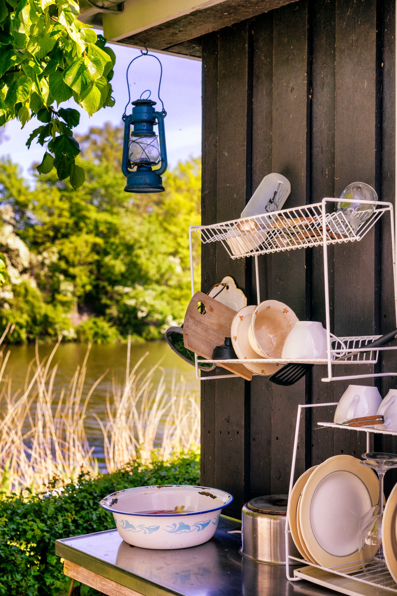 White dish drying rack with plates and bowls on wooden fence with blue lantern hanging above