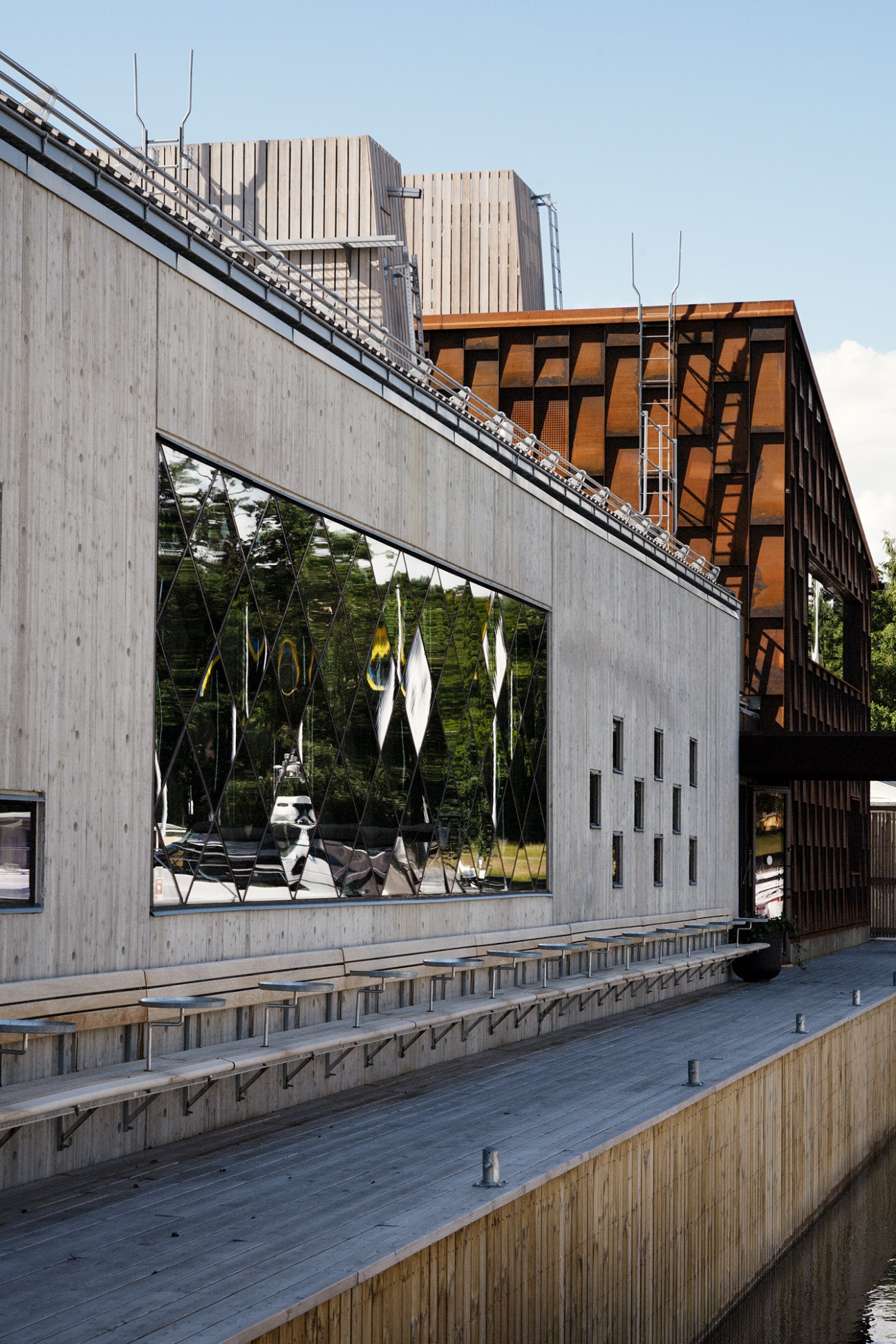 Modern concrete and steel restaurant building with large glass windows and wooden deck overlooking water