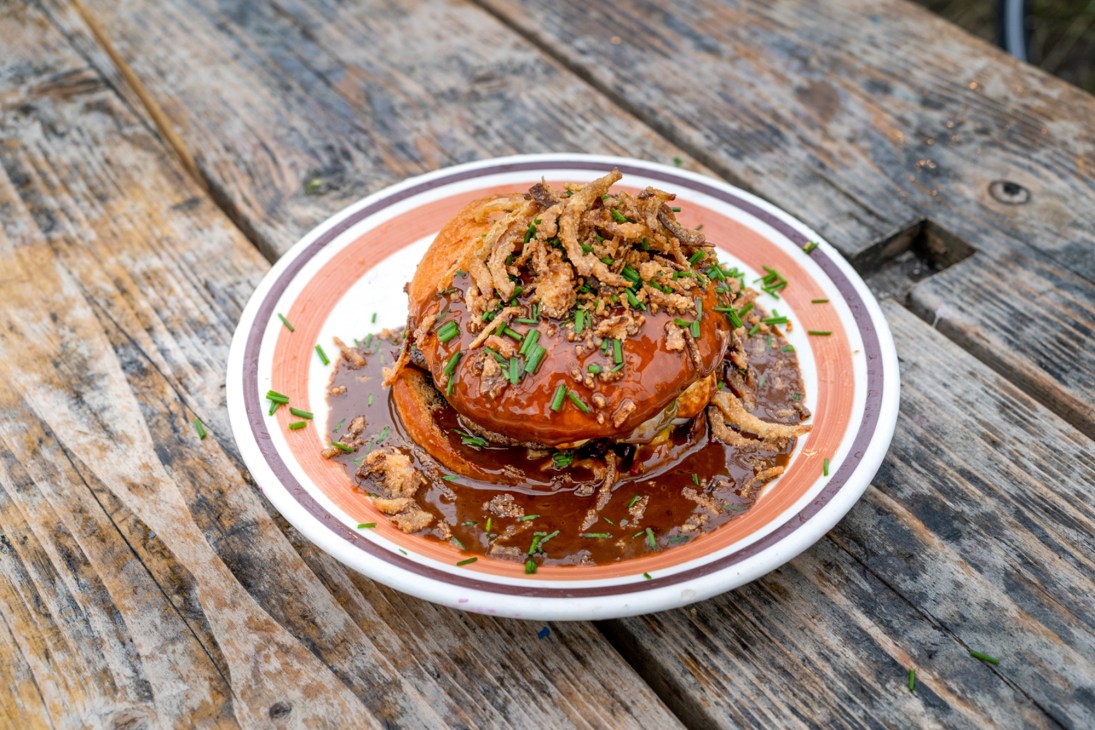 Open-faced beef sandwich with caramelized onions and rich gravy on orange-rimmed plate at outdoor wooden table