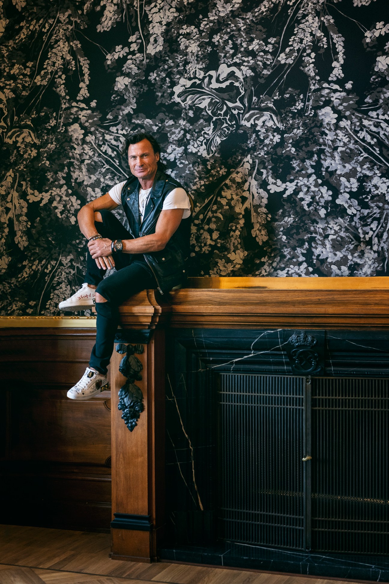 Hotel owner Petter Stordalen sitting casually in black leather vest against ornate floral wallpaper
