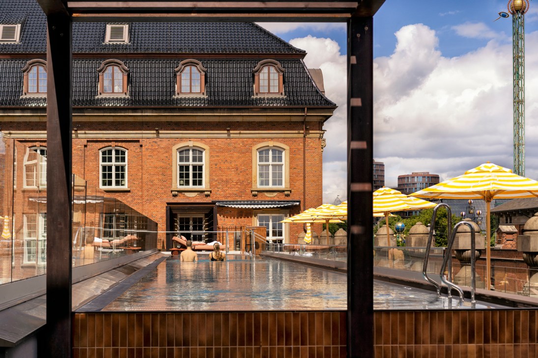Rooftop pool at Villa Copenhagen hotel with yellow striped umbrellas and historic brick building backdrop