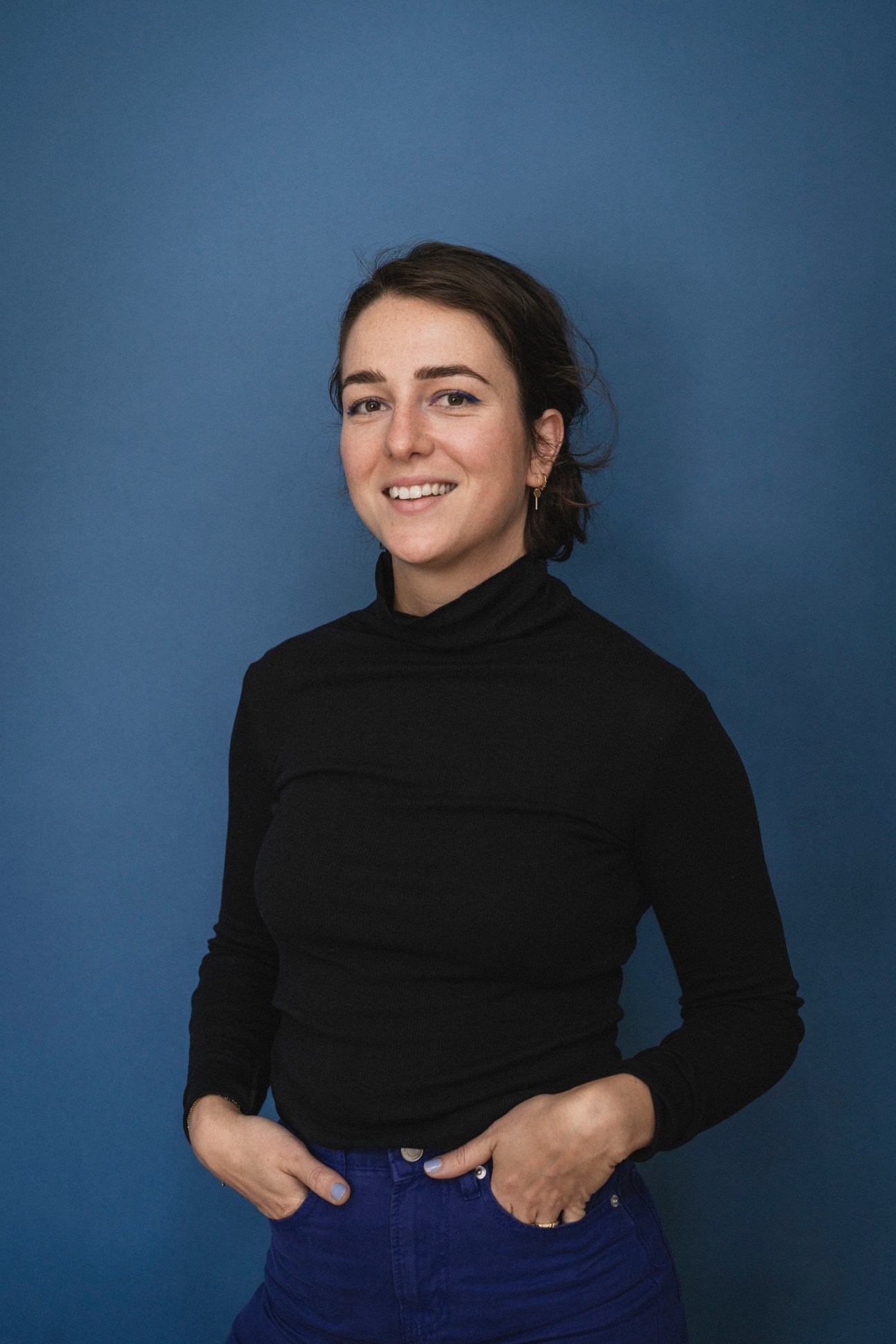 Global launch manager Sedef Güvenç smiling at the camera wearing a black turtleneck against a blue background.
