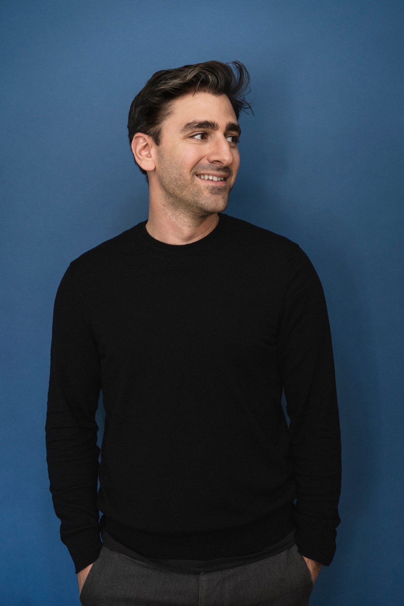Man in black long-sleeved shirt smiling against blue background