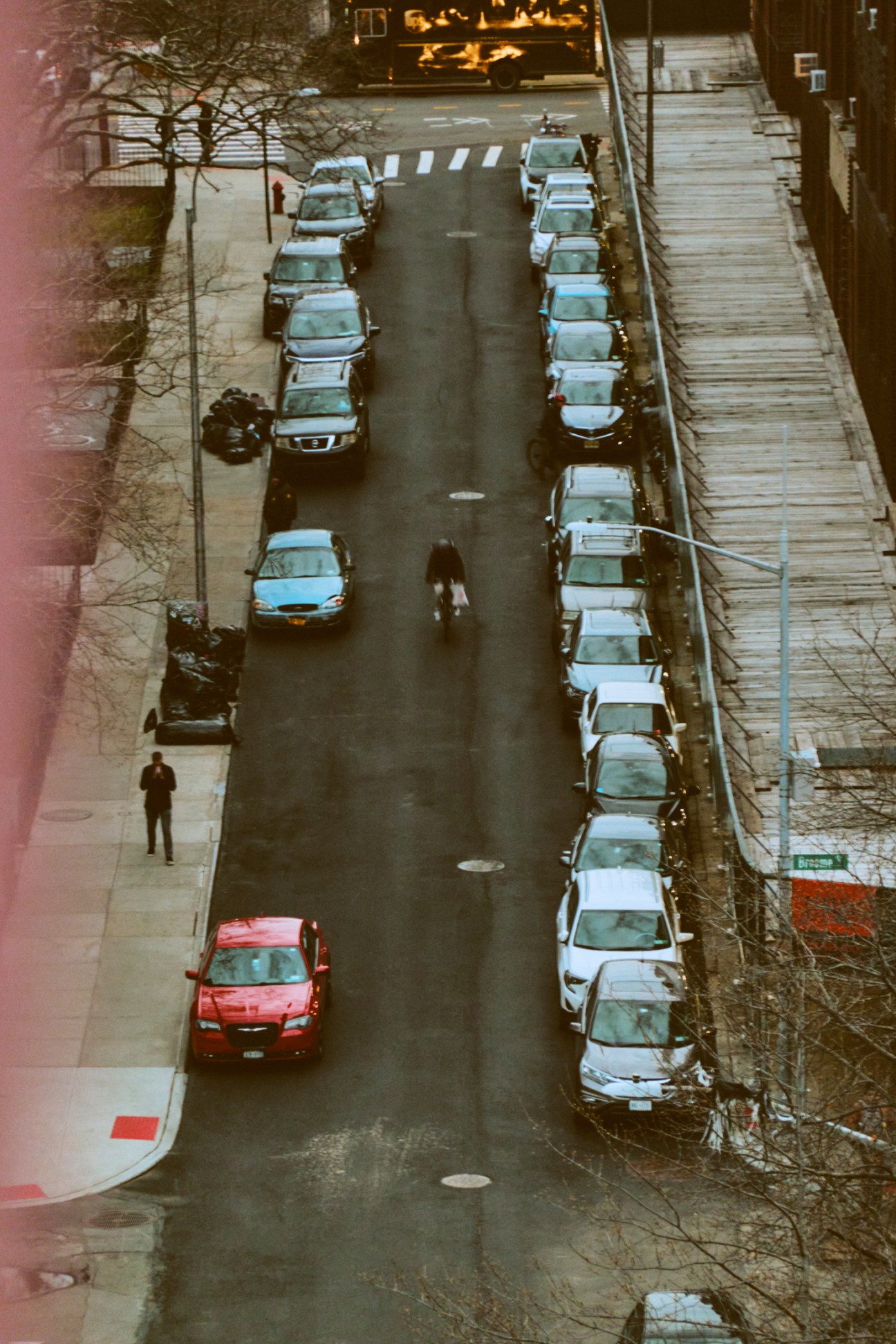 Aerial view of a New York City street with parked cars lining both sides and a yellow taxi among white vehicles.