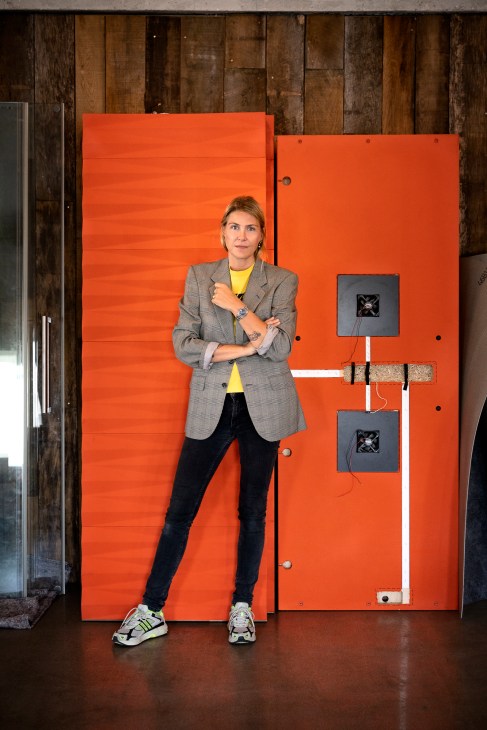 Le Gammeltoft stands with arms crossed in front of a bright orange panel wall with electrical fixtures.