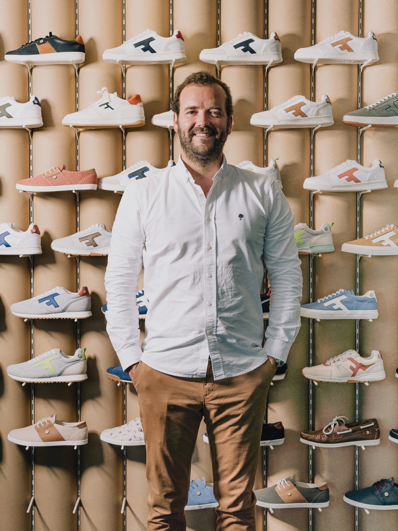 Nicolas Rohr, co-founder of Faguo, stands in front of a wall display of the brand's white sneakers with colored accents.