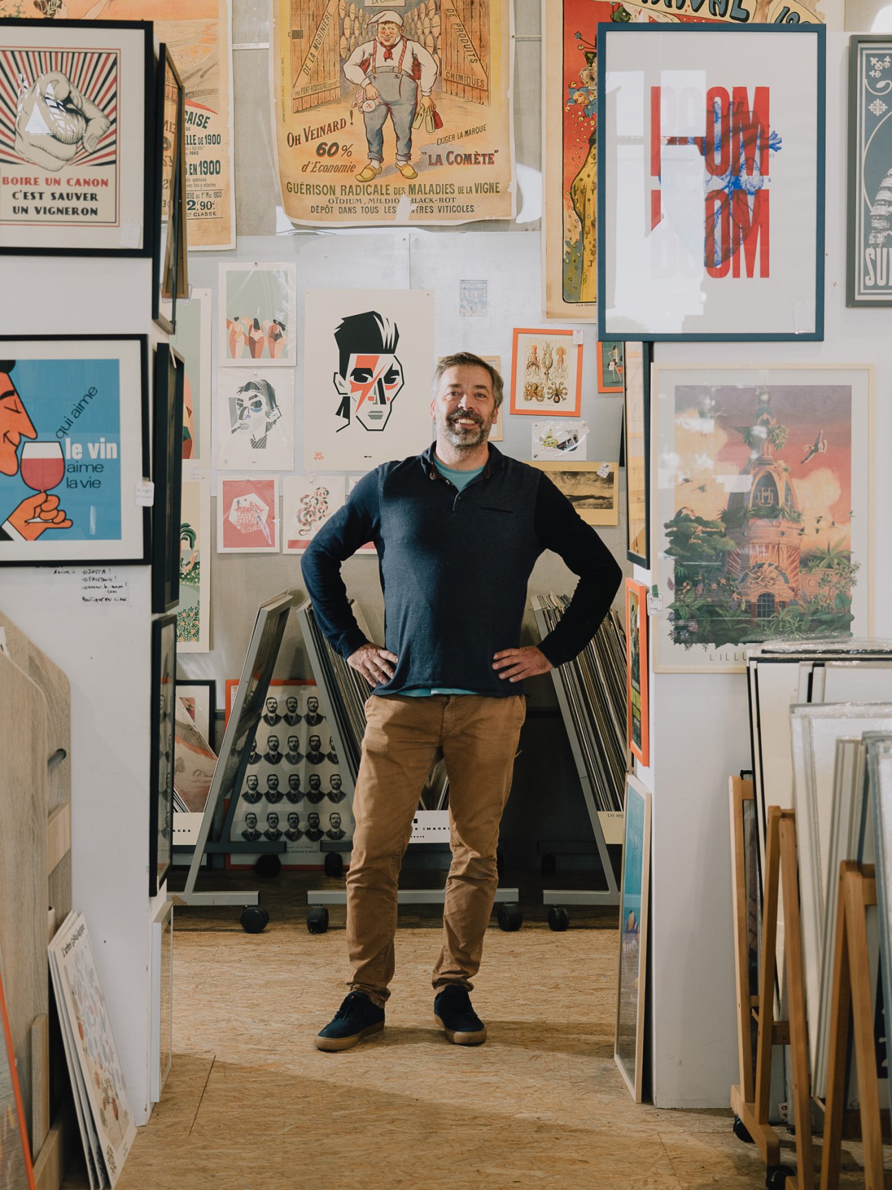 Xavier Thébault standing in his Le Mana shop surrounded by vintage posters and artwork on the walls.
