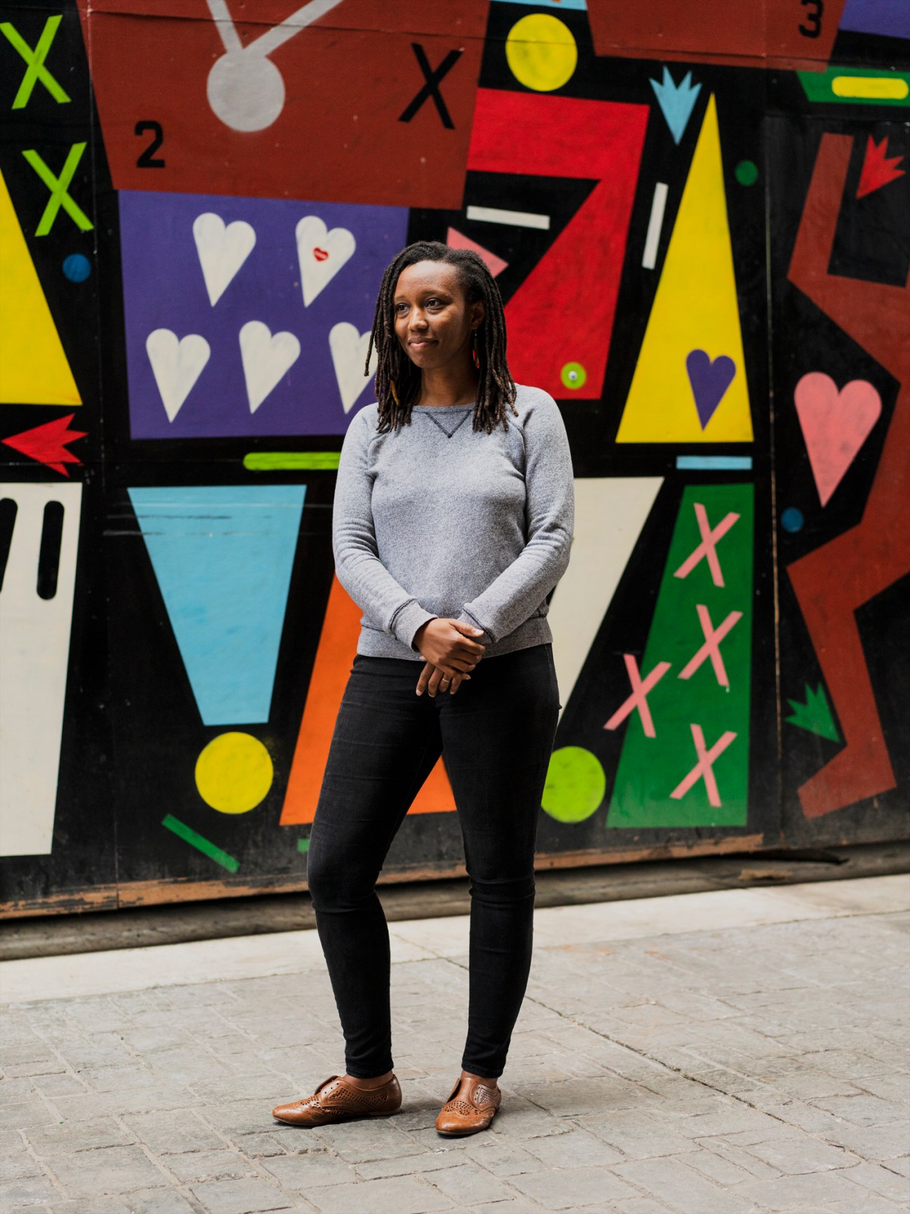 Juana Williams standing in front of a colorful geometric mural with hearts, X's, and various shapes