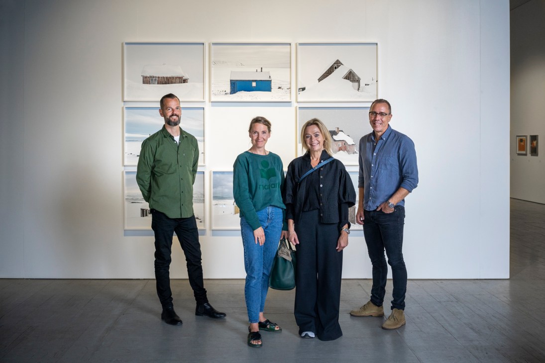 Four people standing in an art gallery in front of framed photographs by Tiina Itkonen on a white wall