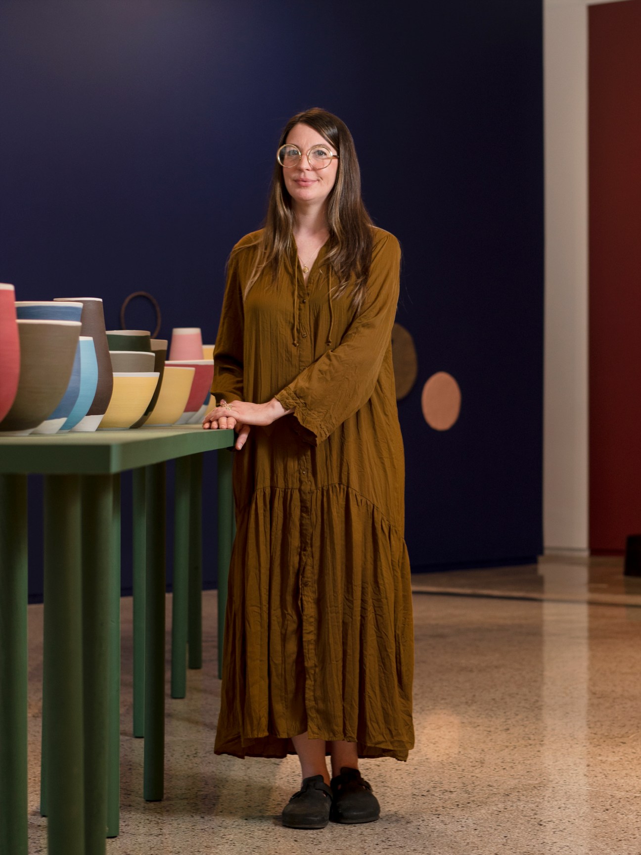 Portrait of gallerist Bridget Finn standing in her gallery space surrounded by colorful ceramic vessels