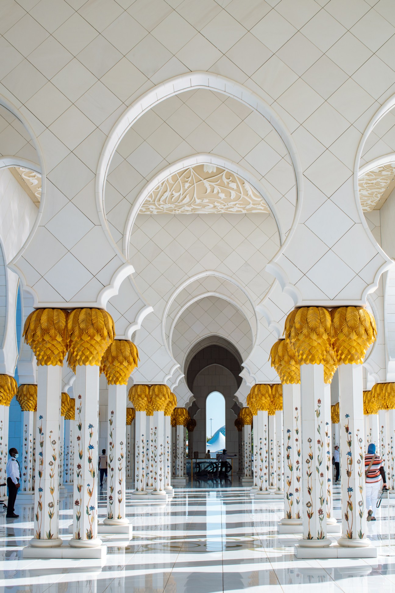 Interior of Sheikh Zayed Grand Mosque with arched white columns, golden chandeliers, and decorative tile work.