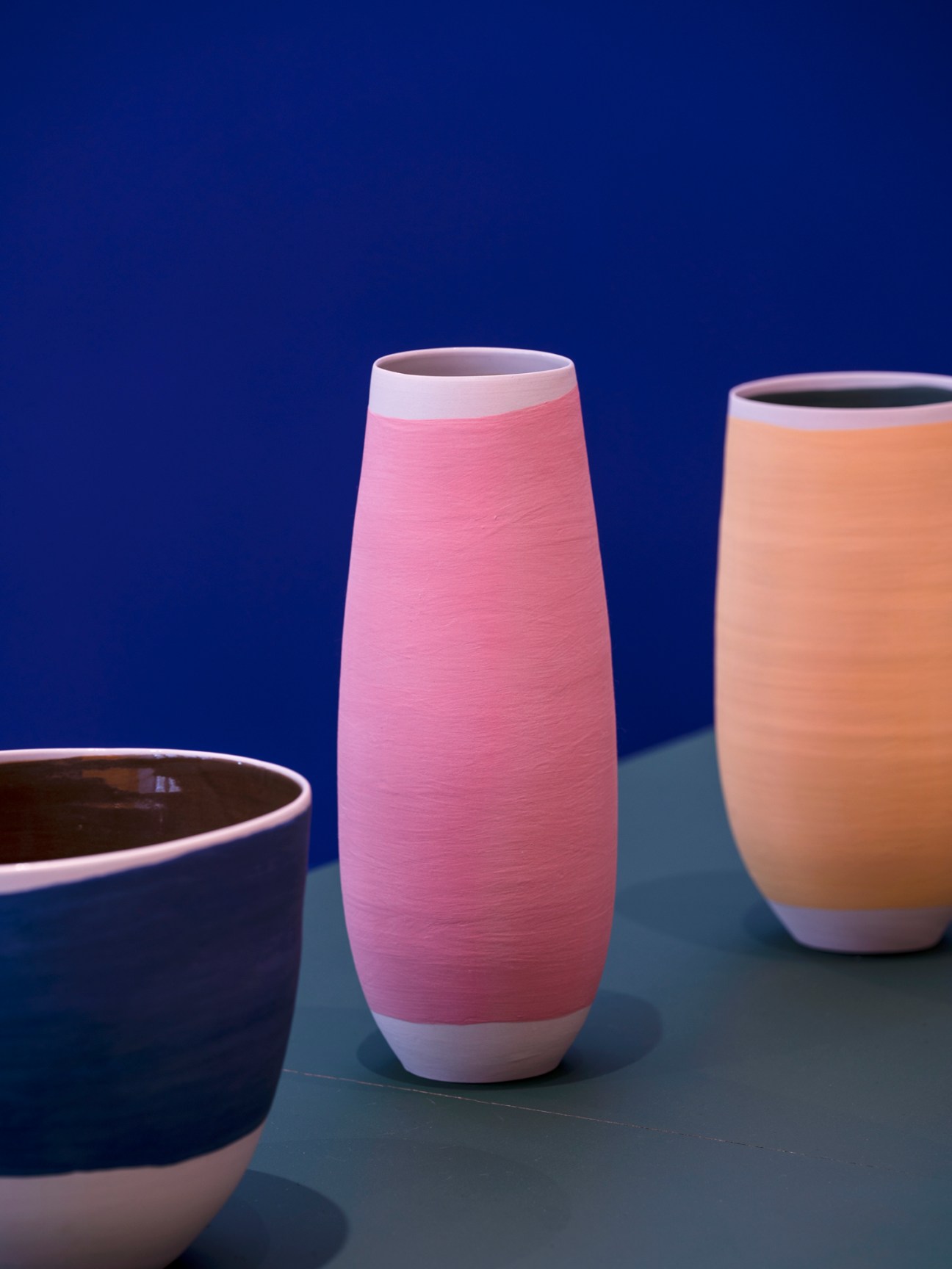 Three ceramic vessels with pink, peach and dark glazes displayed against blue background
