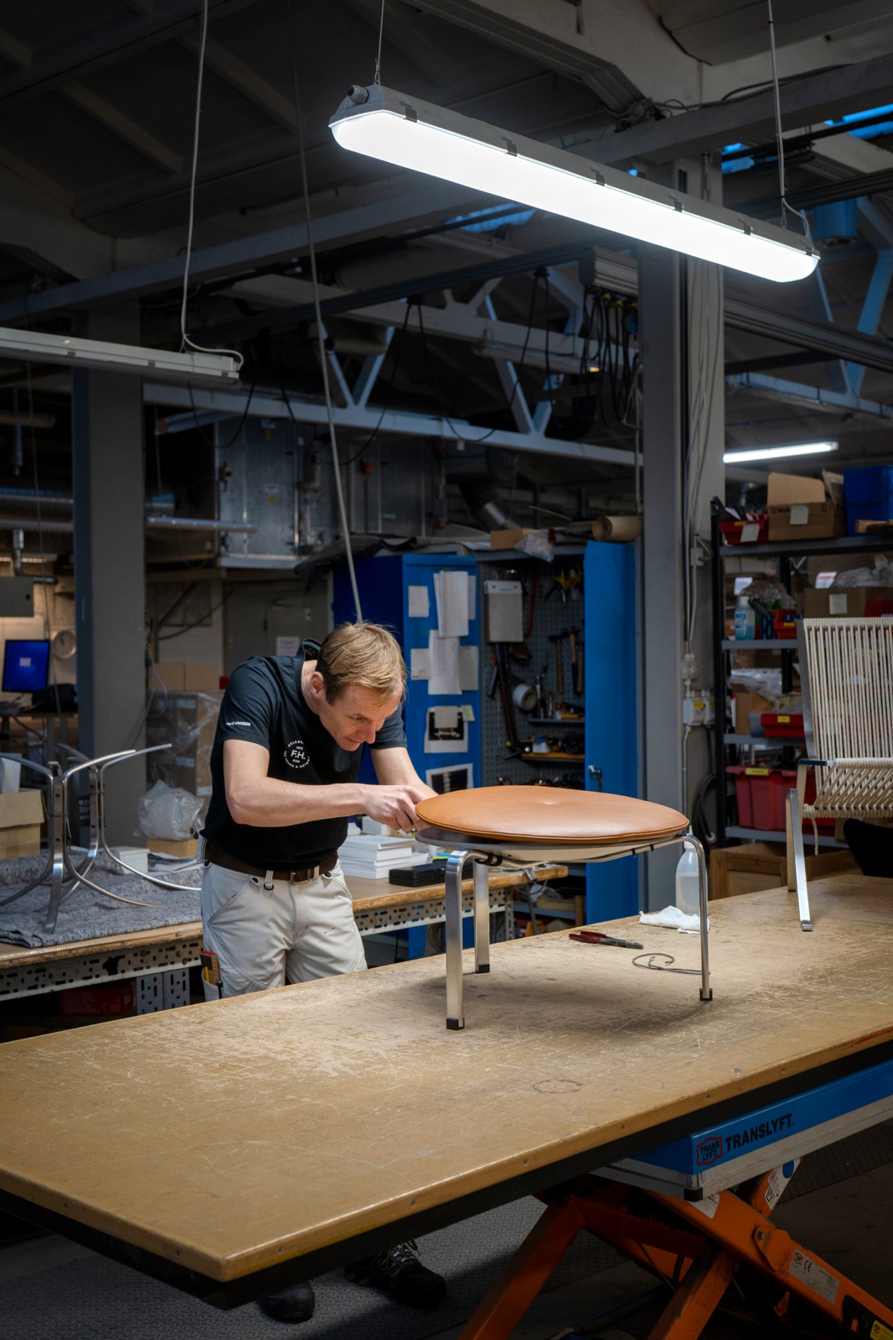 A craftsman in a workshop examining a wooden circular tabletop on metal legs under bright overhead lighting
