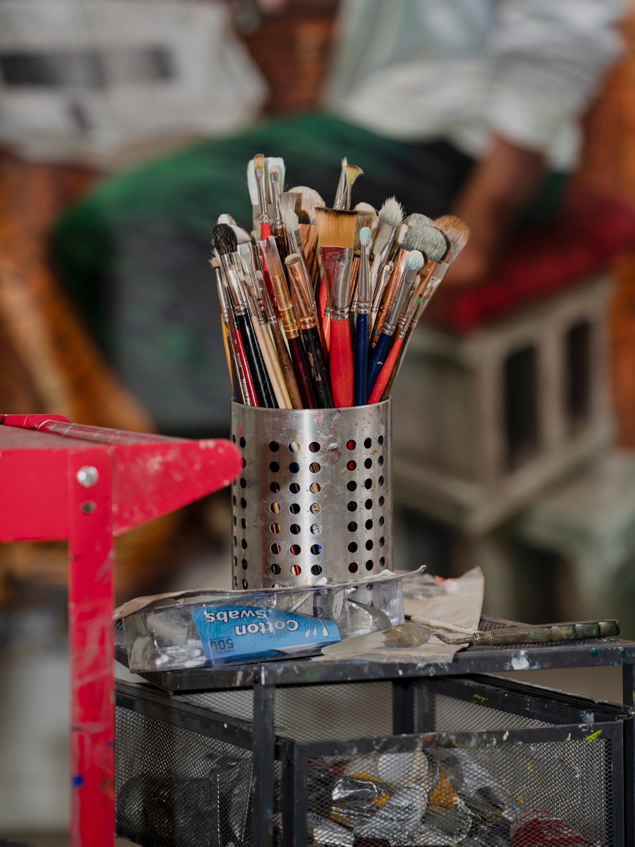Collection of paintbrushes with various colored handles stored in a perforated metal container