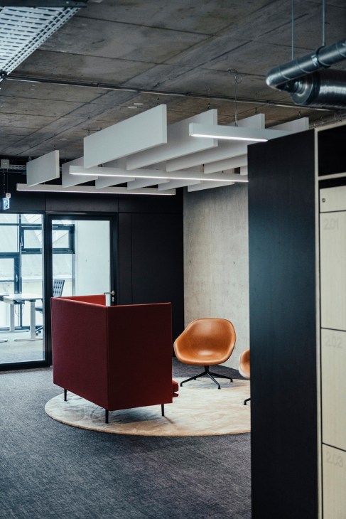 Modern office interior with white pendant lighting, burgundy partition, and cognac-colored chairs on a circular rug.