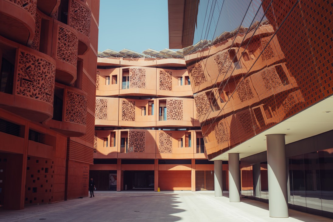 Courtyard of Mohamed bin Zayed University of Artificial Intelligence at Masdar City with red-orange perforated facade and solar panels overhead.