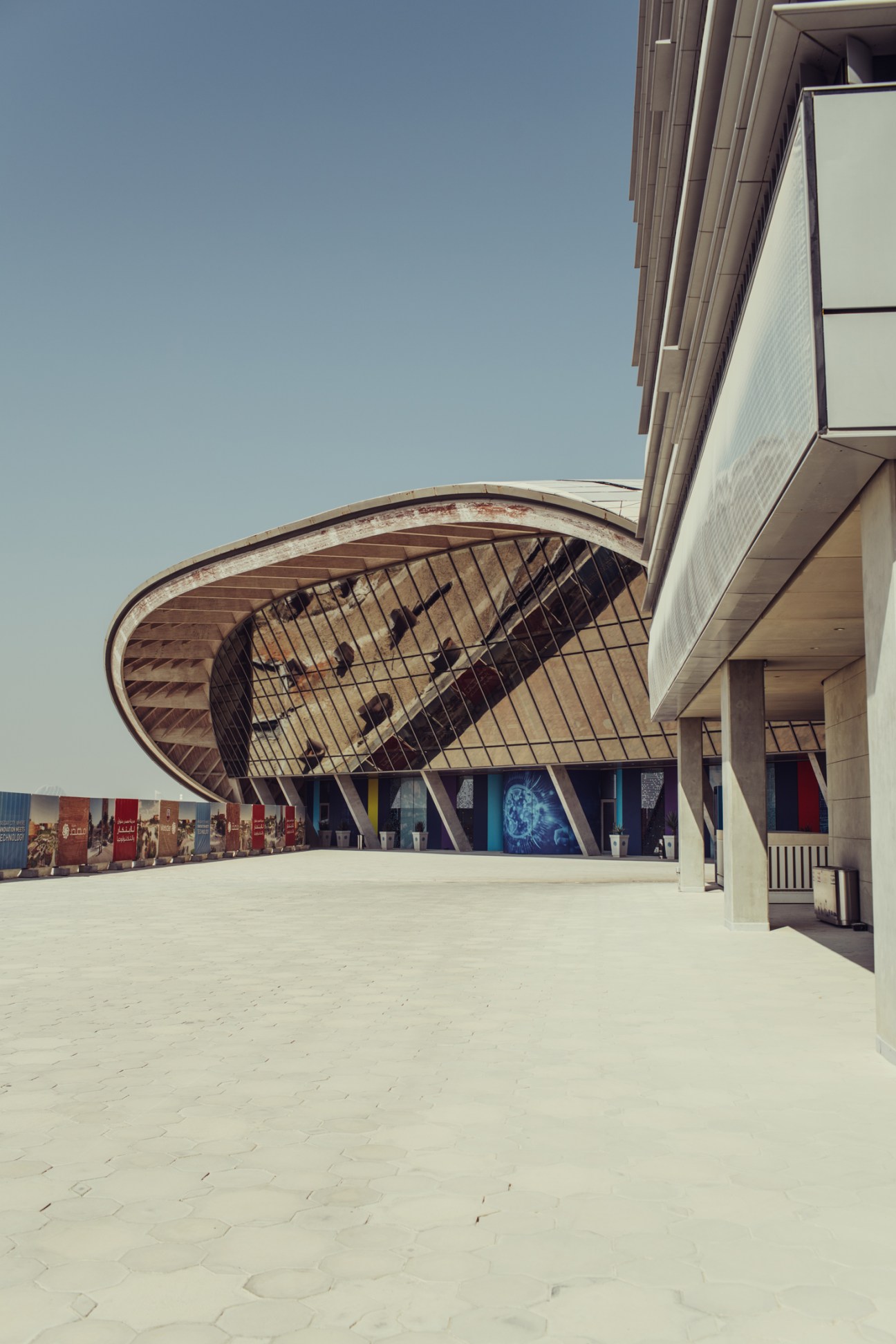 Modern curved architectural structure with mesh dome shelter and white plaza in Masdar City.