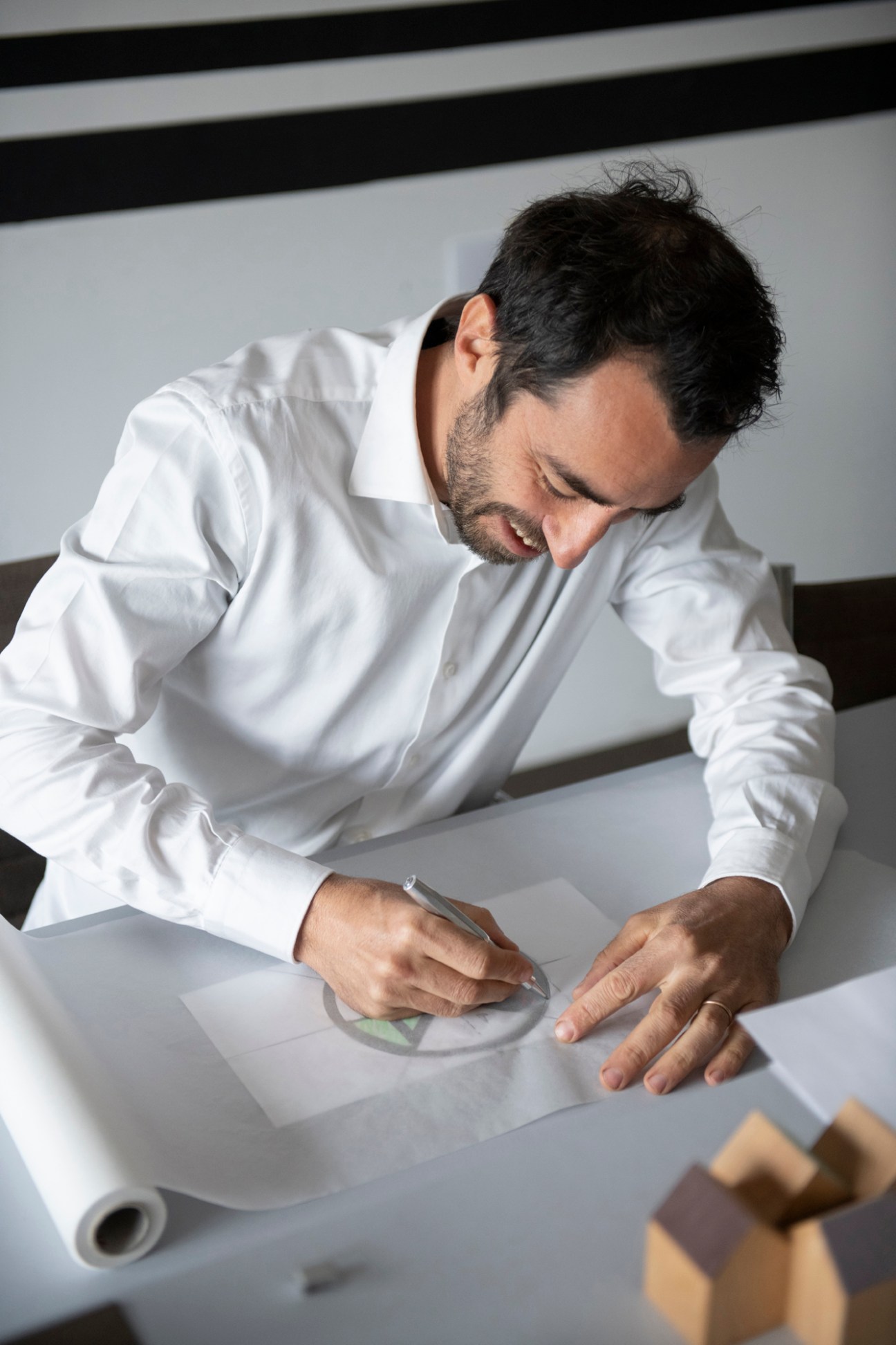 Man in white shirt sketching on paper at a white table with design materials