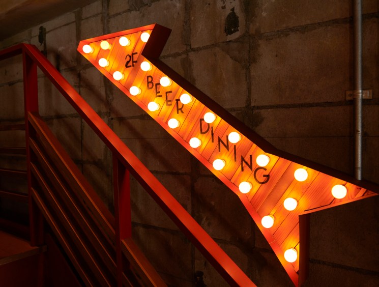 Illuminated orange arrow sign with light bulbs spelling 'BEER DINING' pointing toward restaurant entrance